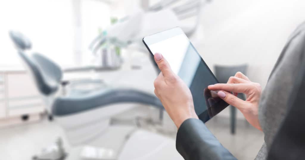 This is a picture of a dentist using an iPad in front of a dental chair.